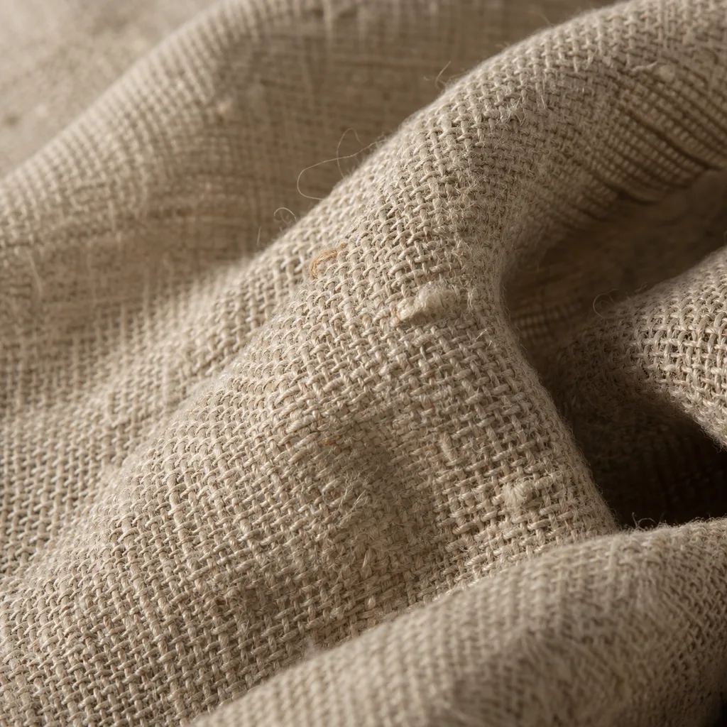 Macro of wet-spun linen showing slubby flax fibres and an open natural weave in warm oatmeal